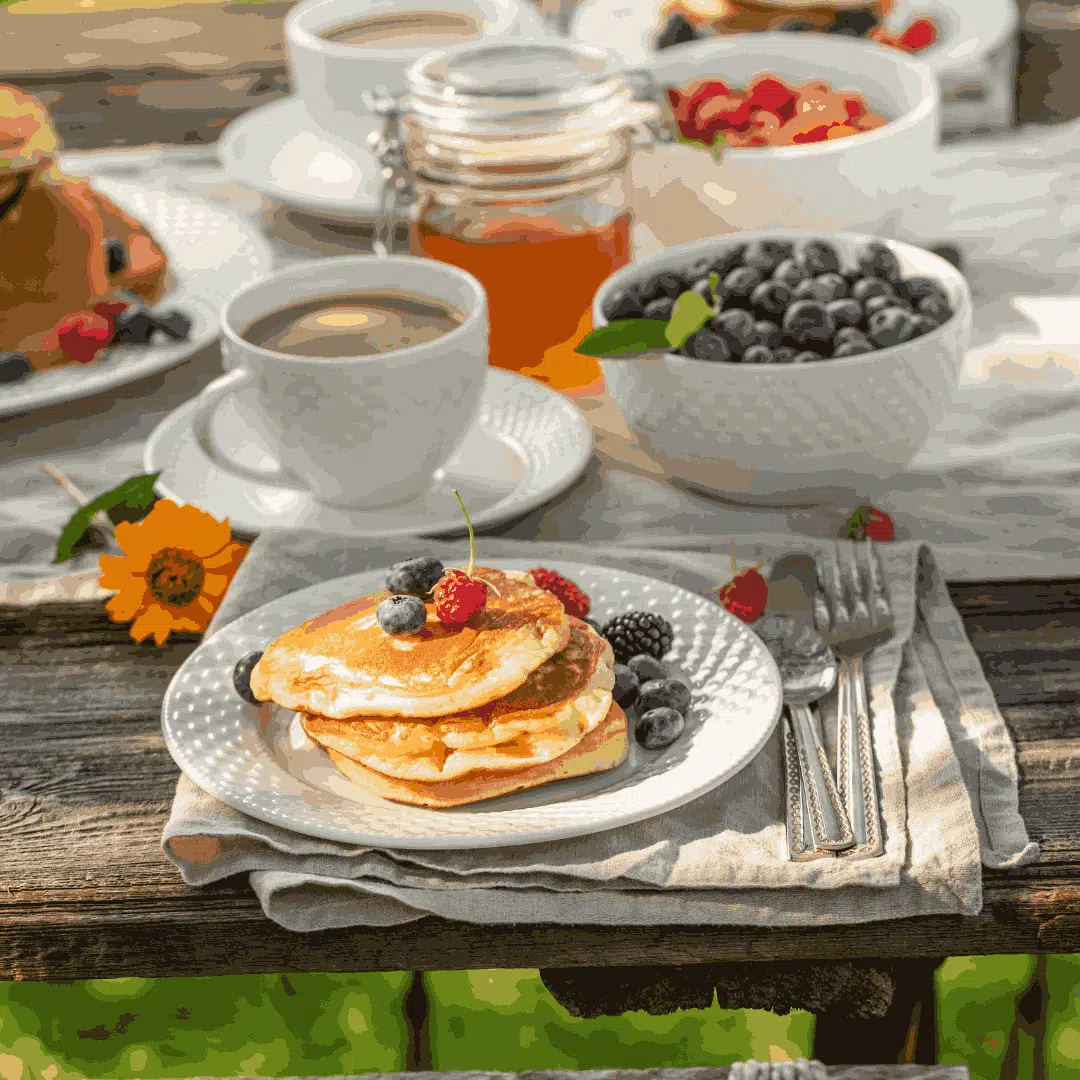 A breakfast table setting with pancakes, berries, coffee, and honey