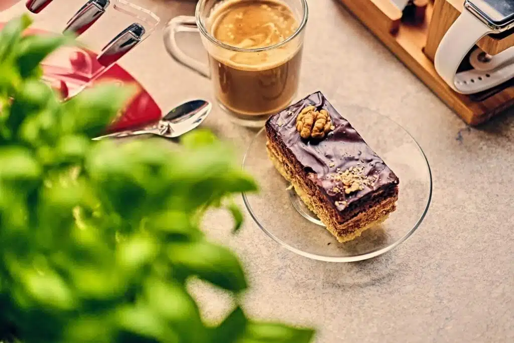 a piece of cake and a cup of coffee on a table with a plant