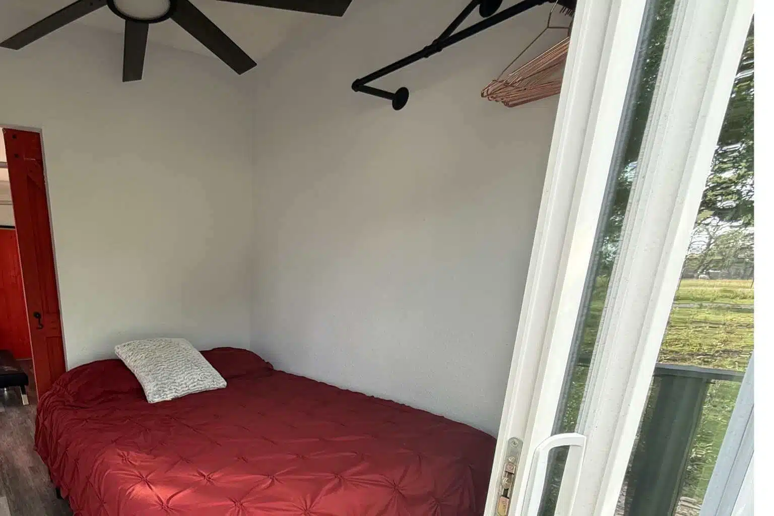 A small room with a single bed, white walls, and a glass door leading to a balcony.