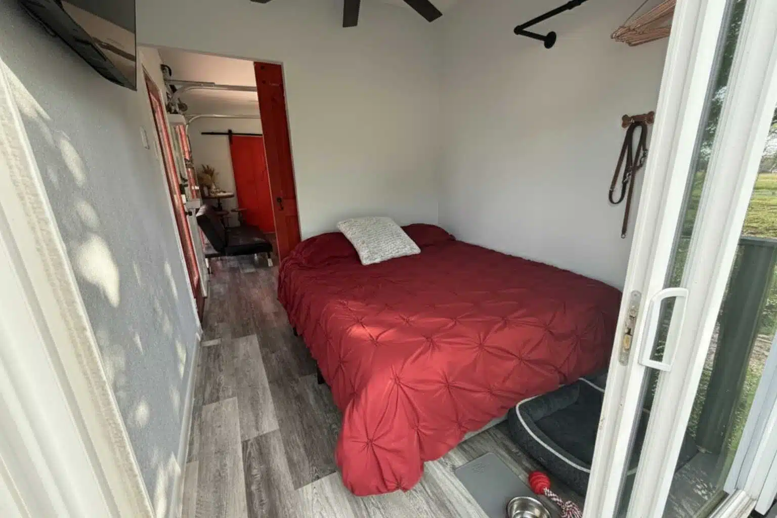 A small room with a red bed, white walls, and a glass door leading outside.
