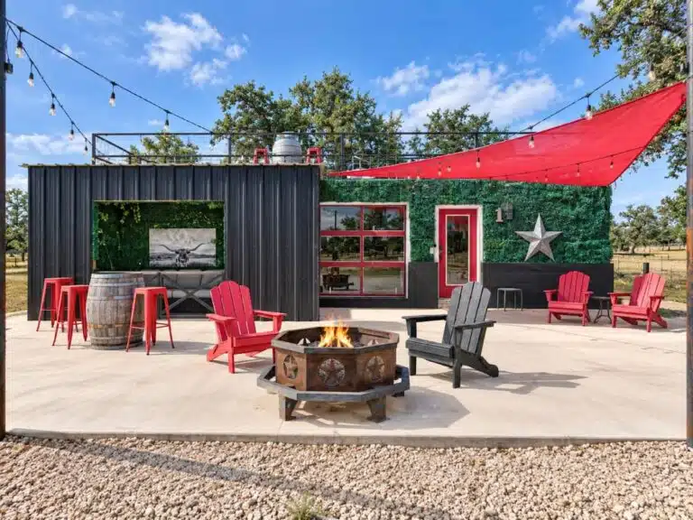 A small outdoor seating area with a fire pit, string lights, and a green wall.